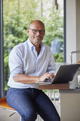 Smiling man with laptop sitting at kitchen island - RBF09010