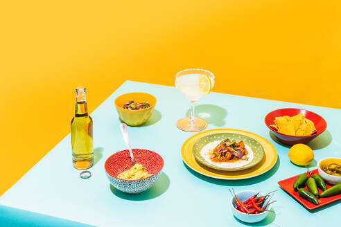 Dishware with nachos and chicken salad placed near bottle of beer and glass of lemonade against yellow background - ADSF38851