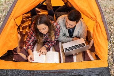 From above couple camping in colorful tent, drinking coffee, reading book and browsing on laptop - ADSF38907