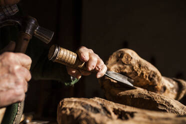 Hände eines anonymen Holzarbeiters, der mit Stechbeitel und Hammer ein Stück Holz bei der Arbeit in einer Tischlerei ausschneidet - ADSF38911