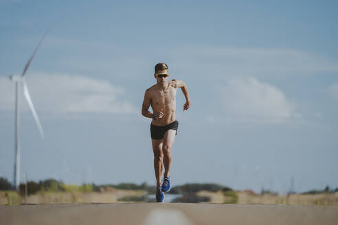 Shirtless fit Sportler läuft auf der Straße vor dem Himmel - MTBF01261