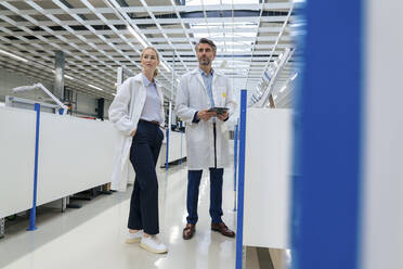 Ingenieur mit Händen in den Taschen neben einem Kollegen, der einen Tablet-PC in einer Fabrik hält - JOSEF13277