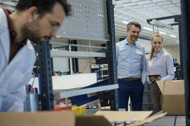 Lächelnder Manager, der einen Tablet-PC in der Hand hält, neben einem Ingenieur, der in einer Fabrik arbeitet - JOSEF13287