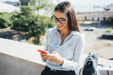 Happy businesswoman using smart phone leaning on wall - OYF00777