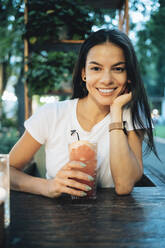 Glückliche Frau mit einem Glas Cocktailgetränk am Tisch in einem Straßencafé - OYF00790