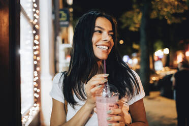 Glückliche Frau mit Smoothie auf dem Fußweg - OYF00794