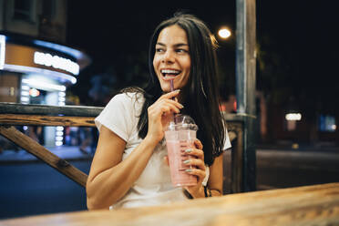 Fröhliche Frau mit Smoothie in einem Straßencafé bei Nacht - OYF00800
