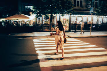 Frau mit Smoothie beim Überqueren der Straße in der Nacht - OYF00805