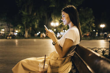 Frau mit Smartphone auf einer Parkbank sitzend bei Nacht - OYF00807