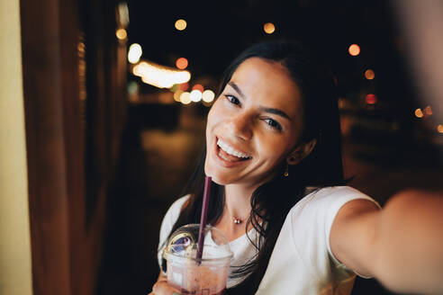 Fröhliche Frau mit Smoothie nimmt Selfie bei Nacht - OYF00809