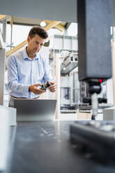 Älterer Ingenieur prüft Maschinenteil mit Laptop in der Fabrik - DIGF18845