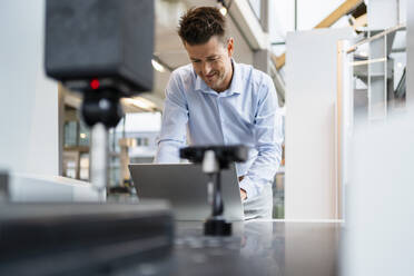 Lächelnder Techniker bei der Arbeit am Laptop in der Fabrik - DIGF18846