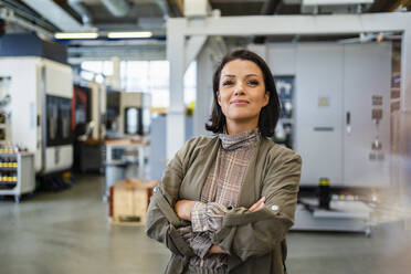 Confident businesswoman with arms crossed standing at factory - DIGF18865