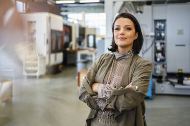 Smiling businesswoman with arms crossed standing at factory - DIGF18866