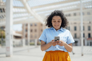 Woman with curly hair text messaging through mobile phone - JOSEF13329