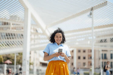 Happy woman holding smart phone on sunny day - JOSEF13331