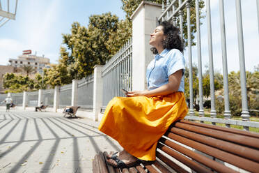 Lächelnde Frau genießt das Sonnenlicht auf einer Bank im Park - JOSEF13343