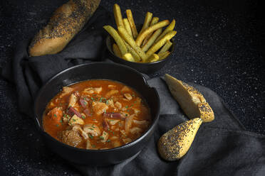 Von oben schmackhafte Callos a la madrilena in schwarzer Schale neben Pommes frites und Brot mit Kernen - ADSF38978