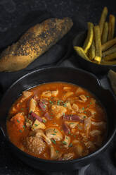 Von oben schmackhafte Callos a la madrilena in schwarzer Schale neben Pommes frites und Brot mit Kernen - ADSF38979