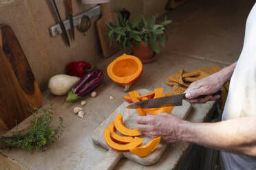 Hands of man cutting pumpkin on board in kitchen - SVKF00571