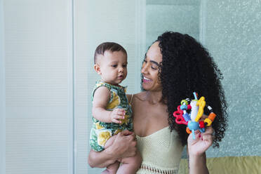 Happy woman holding toy playing with son at home - PNAF04542