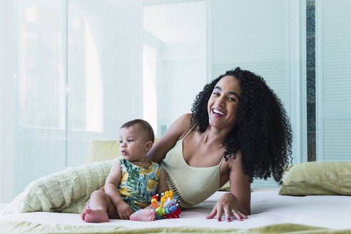 Cheerful woman with baby boy sitting on bed at home - PNAF04543