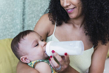 Happy woman feeding baby boy with bottle at home - PNAF04545