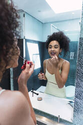 Frau beim Schminken vor einem Spiegel zu Hause - PNAF04559