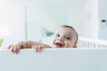 Happy baby boy playing in crib at home - PNAF04561