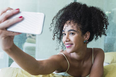 Glückliche schöne Frau mit lockigem Haar nimmt Selfie durch Smartphone zu Hause - PNAF04574