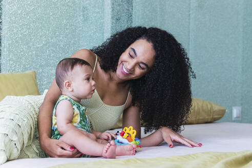 Happy woman with baby boy sitting on bed at home - PNAF04584