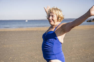 Smiling senior woman with arms outstretched standing at beach - UUF27315