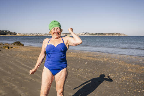 Glückliche ältere Frau beim Muskeltraining am Strand - UUF27324