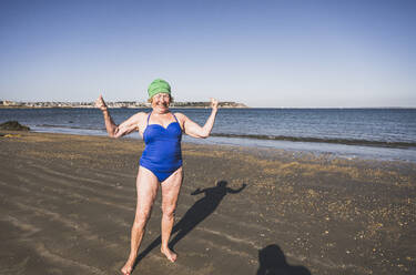 Smiling elderly woman flexing muscles at beach - UUF27326