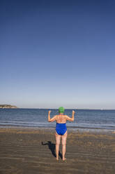 Woman looking at sea and flexing muscles on sunny day - UUF27328