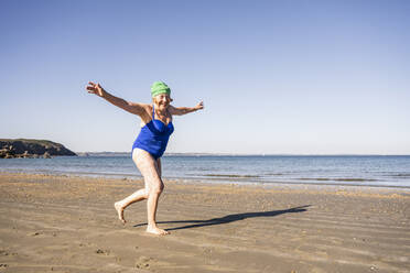 Unbeschwerte ältere Frau, die an einem sonnigen Tag am Strand Spaß hat - UUF27332