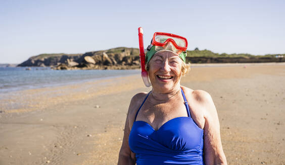 Cheerful woman wearing diving goggles and snorkel mask at beach - UUF27356