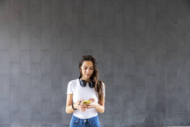 Frau mit Smartphone vor grauer Wand - WPEF06500