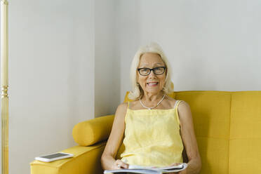 Glückliche ältere Frau, die zu Hause auf einem gelben Sofa sitzt - SEAF01250