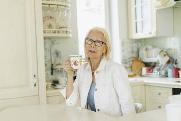 Frau hält Tasse in der Küche sitzend zu Hause - SEAF01259