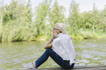 Senior woman day dreaming sitting on jetty near lake - SEAF01283