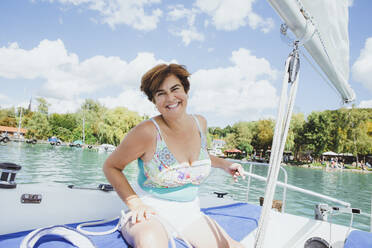 Glückliche Frau, die ihren Urlaub auf einem Segelboot sitzend genießt - AANF00317