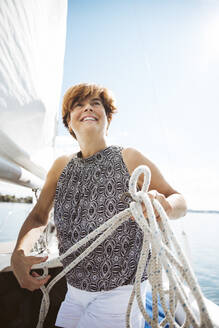 Smiling woman holding rope standing on sailboat - AANF00320