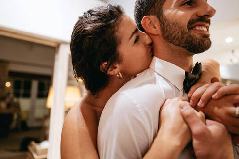 Zärtliches junges Paar, das zusammen in seinem Hotelzimmer steht. Glückliche junge Frau, die ihren Mann auf den Hals küsst. Romantisches junges Paar, das einen Flitterwochenurlaub in einem Luxushotel genießt. - JLPPF00992