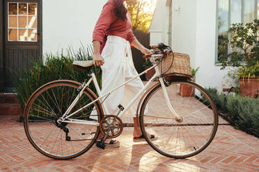 Young woman pushing a bicycle outdoors at a hotel. Anonymous young tourist woman going out for a bike ride while on a luxury vacation. Young female biker walking alone during the day. - JLPPF01017