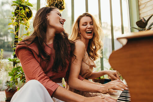 Zwei fröhliche Freundinnen, die zusammen singen und Klavier spielen. Zwei glückliche junge Frauen, die lächelnd ihr Lieblingslied singen. Beste Freundinnen, die in den Sommerferien Spaß haben. - JLPPF01100