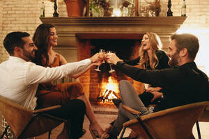 Vier glückliche Freunde, die vor einem Kamin in einem Luxushotel sitzen und feiern. Zwei fröhliche Paare, die mit Weingläsern anstoßen. Eine Gruppe von Freunden, die gemeinsam einen Wochenendausflug genießen. - JLPPF01130