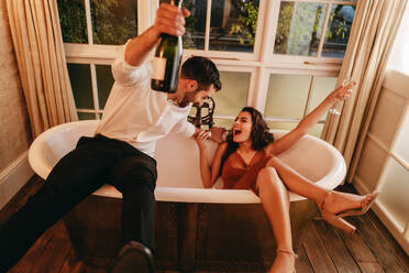 Fröhliches junges Paar, das in einer Badewanne Sekt trinkt. Romantisches junges Paar, das seinen Flitterwochenurlaub in einem Luxushotel genießt. - JLPPF01194