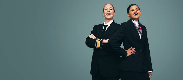 Flugkapitän und Stewardess lächeln in die Kamera, während sie zusammen stehen. Fröhlicher Pilot und Flugbegleiterin in ihren Uniformen vor einem Studiohintergrund. - JLPPF01273