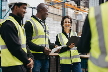 Mature woman laughing cheerfully during a staff meeting with her colleagues in a distribution warehouse. Group of happy employees working together in a fulfillment centre. - JLPPF01313